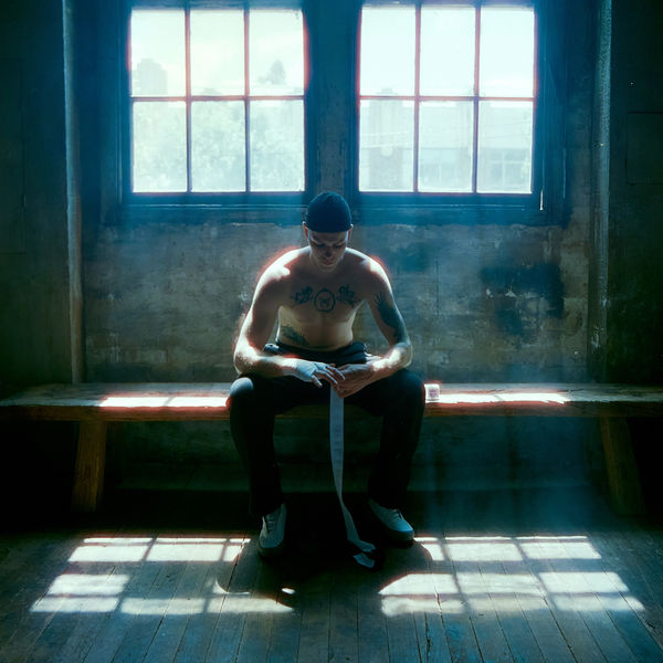 Boxer sitting on a bench wrapping his hands in a sunlit warehouse gym