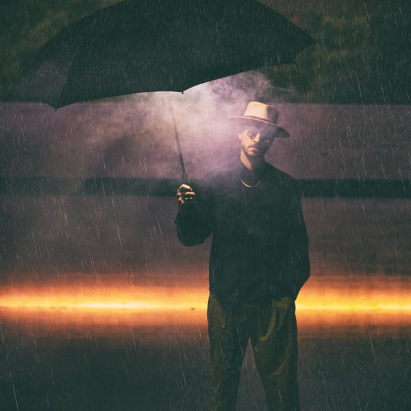 Portrait of a man holding an umbrella against a glowing horizon in the rain