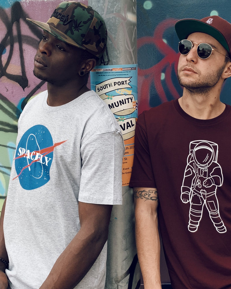 Two people in Spacely globe and astronaut tees against a graffiti wall