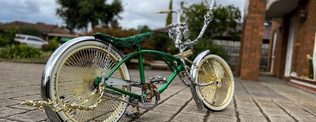 Green and chrome lowrider bicycle with spoked wheels outside a brick house