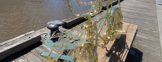 Gold-plated show lowrider bicycle displayed on a pier at the water's edge