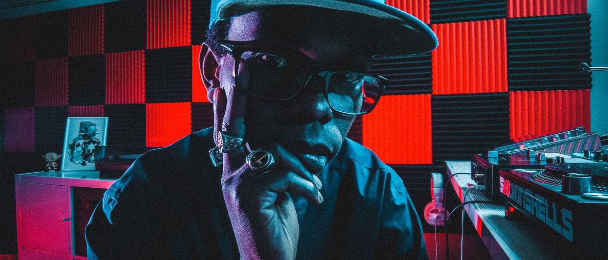 Henry Skillz in a studio lit red and teal, checkered acoustic panels behind him