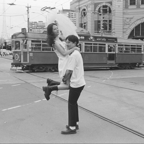 Black and white street photograph by Scott Ransley showing couple embracing at Flinders Street Station with heritage tram and Melbourne CBD in background