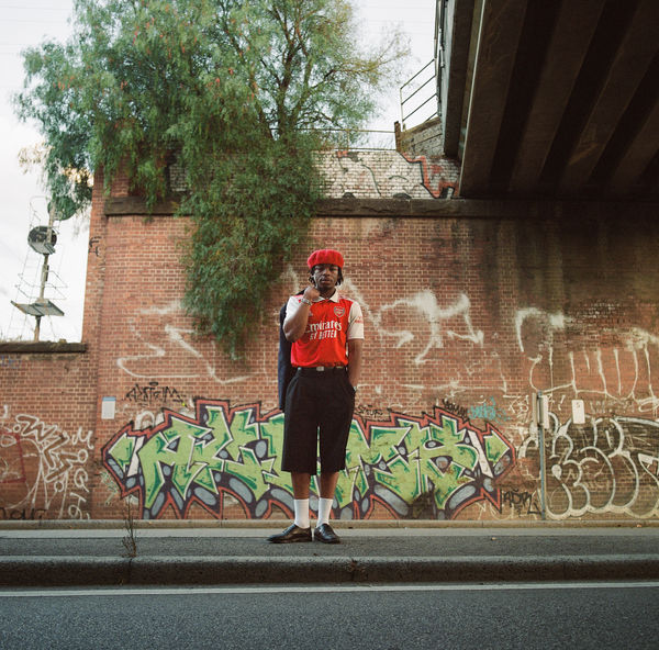 Person in a red singlet standing against a graffiti wall under an overpass