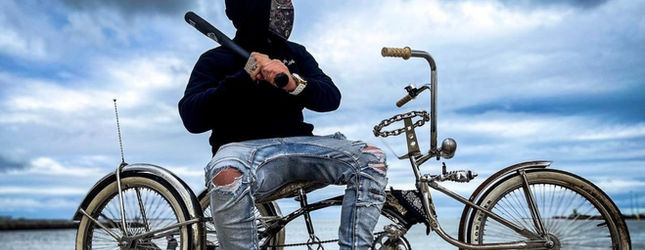 Rider in a balaclava on a lowrider bicycle against a cloudy sky