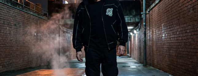 Figure in a black Spacely tracksuit in a laneway with steam rising