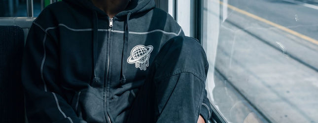 Person in a black Spacely zip hoodie beside a window