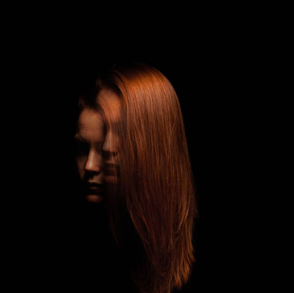 Low-key portrait of a woman with red hair emerging from darkness