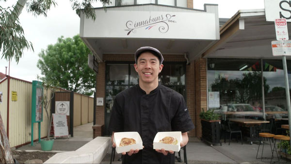 Baker holding two boxes of cinnamon scrolls outside his shop