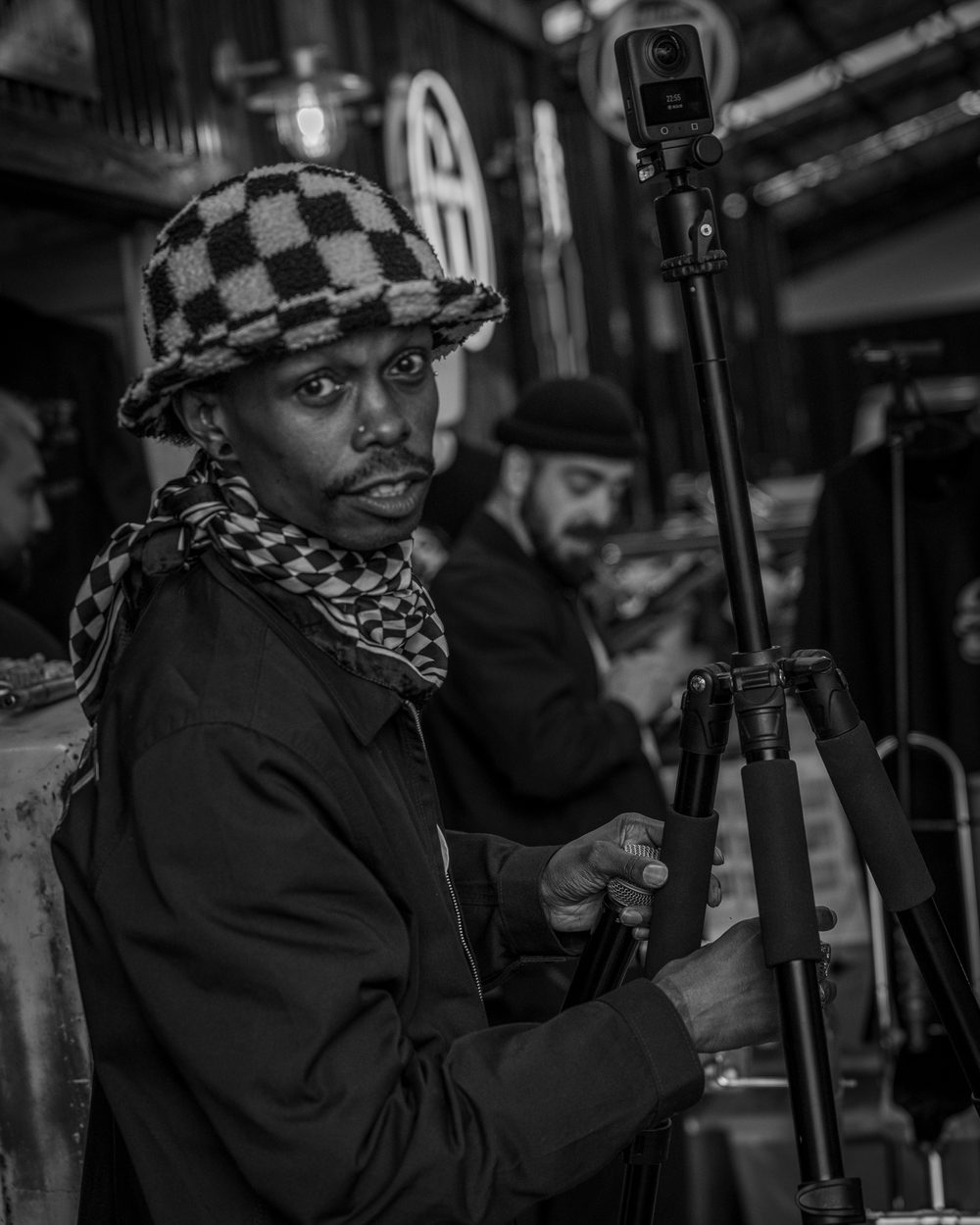 Henry Skillz behind a camera on a tripod in a workshop, shot in black and white