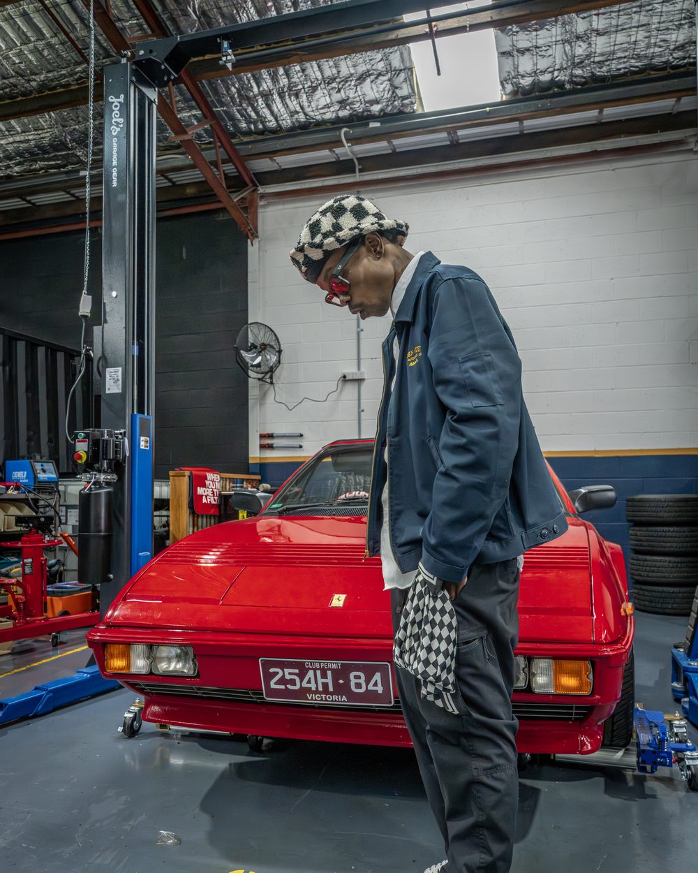 Henry Skillz beside a red sports car on a hoist in a Melbourne workshop