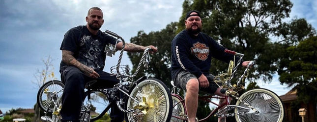 Two Low Ballers Mafia riders on custom lowriders under an open sky