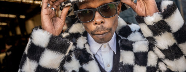 Man in a black and white checked fur coat and sunglasses