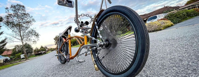 Yellow lowrider bicycle with a tall sissy bar on a suburban road