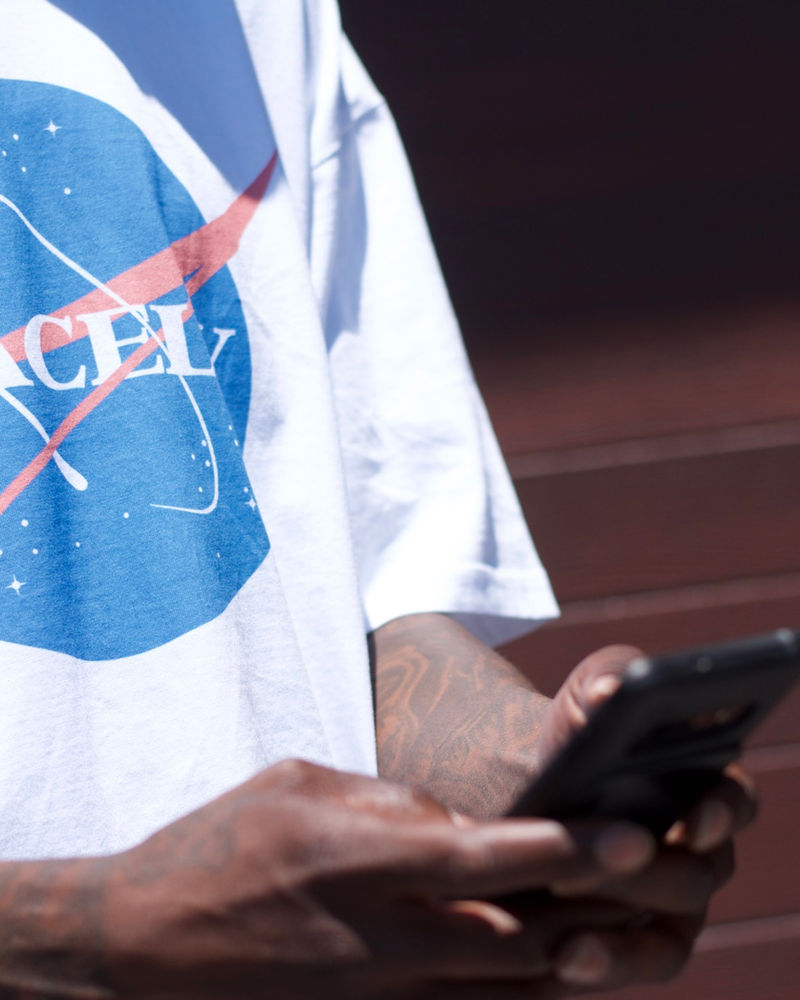 Man in a white Spacely tee checking his phone on the street