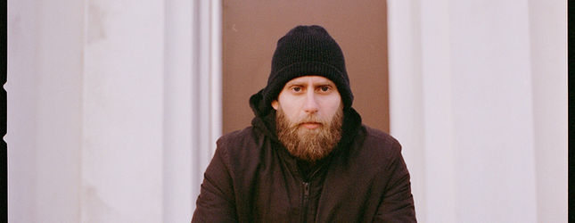 Portrait of a man in a beanie and jacket against a pale wall
