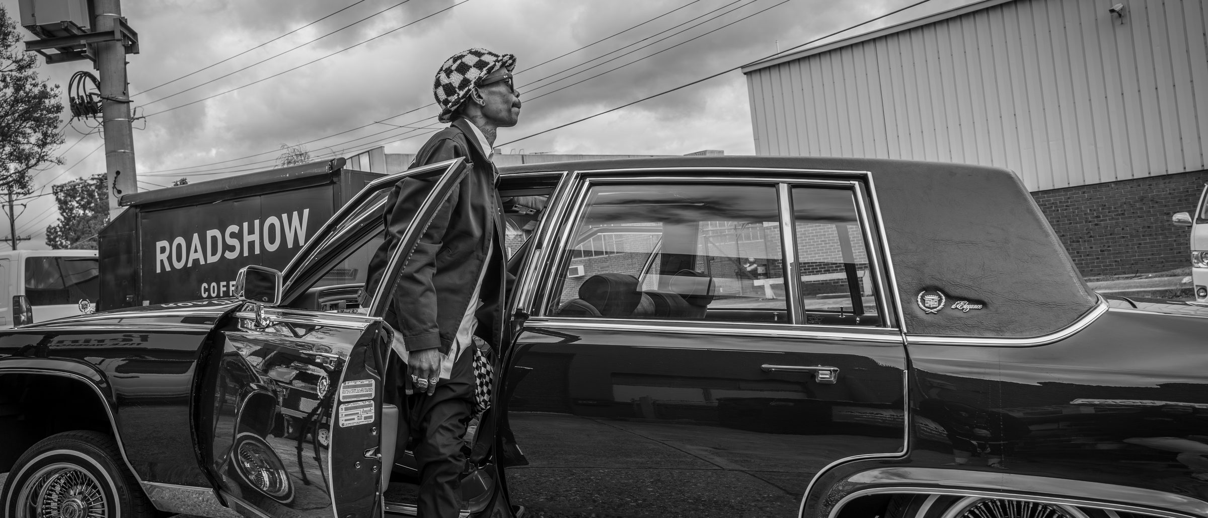 Henry Skillz stepping out of a black Cadillac lowrider on a Melbourne industrial street
